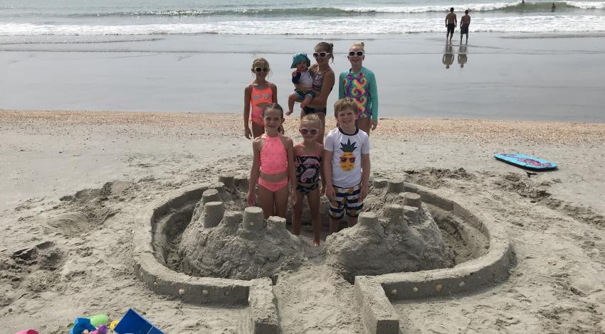 six kids and a baby in and around large sandcastle