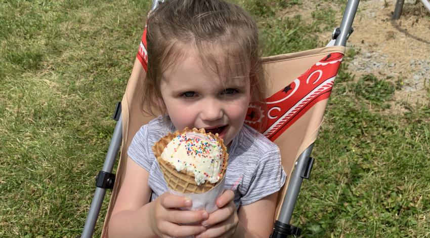Little girl sits in stroller, holding big ice cream cone.