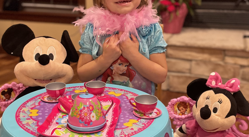 little girl in boa and tiara having tea with stuffed Mickey and Minnie Mouse