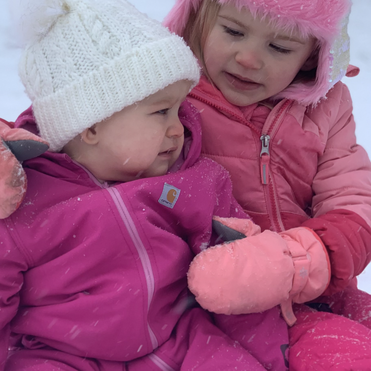 little girl and baby sitting in the snow