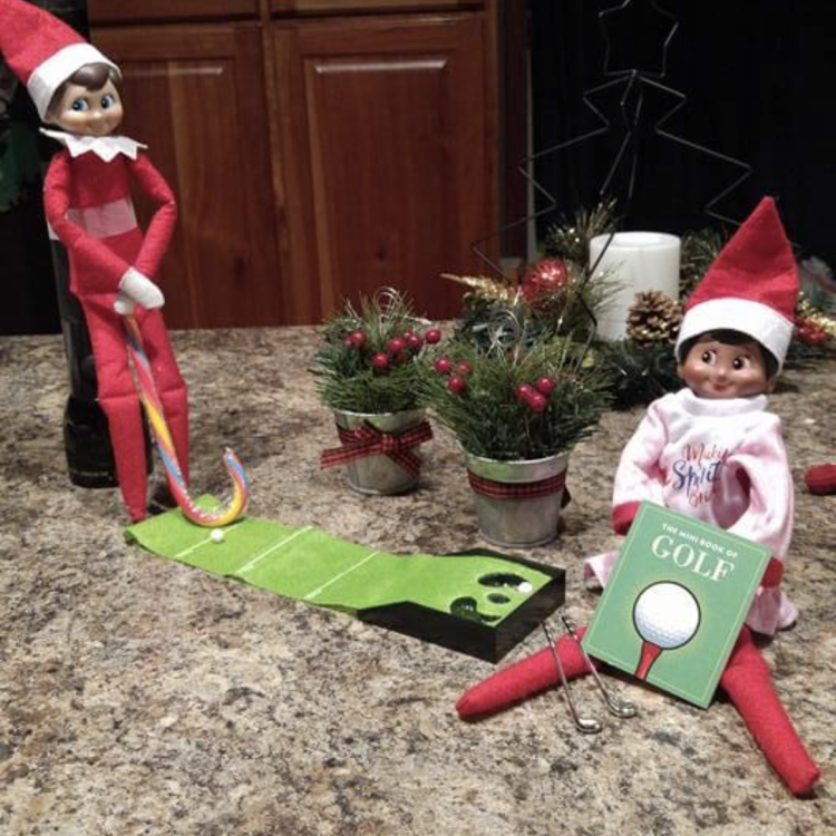 Elf on the Shelf holds upside-down candy cane by tiny putting mat