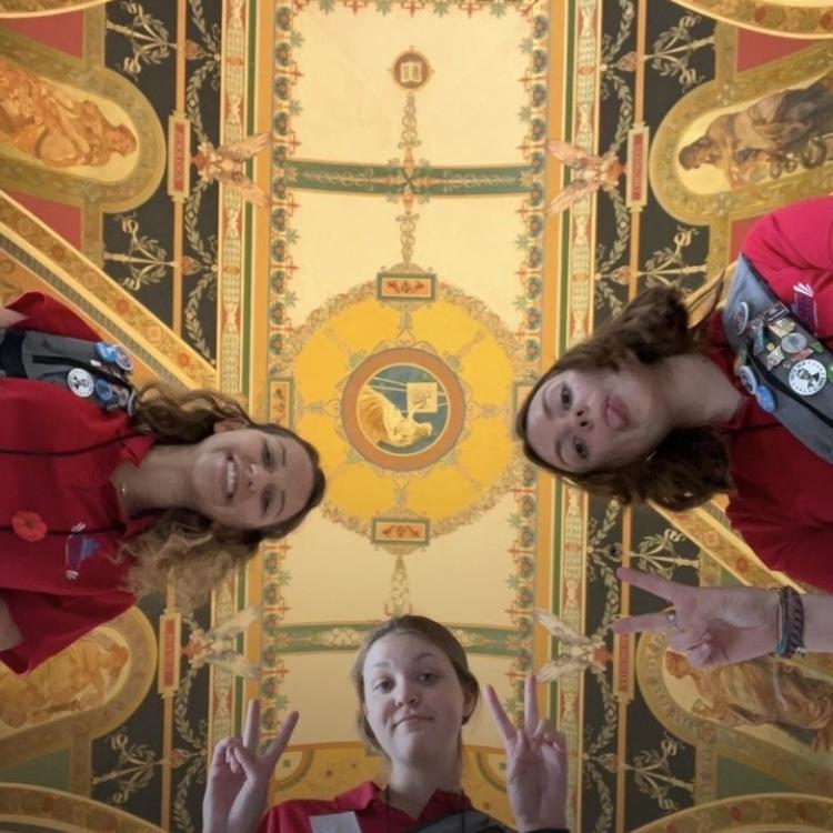 Photo of three teenage girls, shot from below, with ornate ceiling above