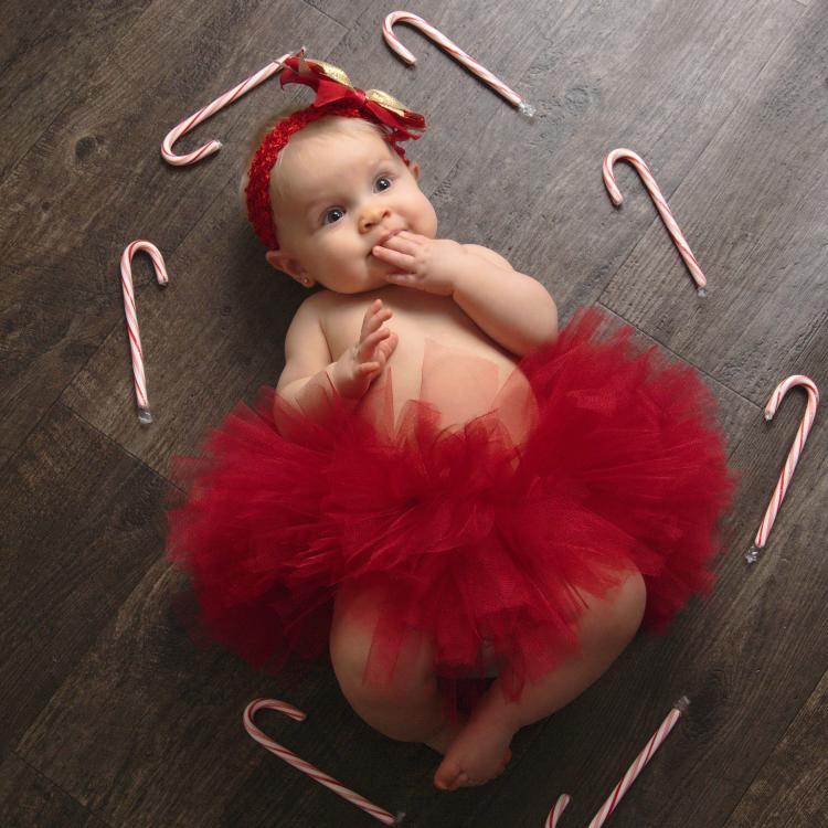 Baby girl in fluffy red tutu, ringed by candy canes and sucking on her fingers