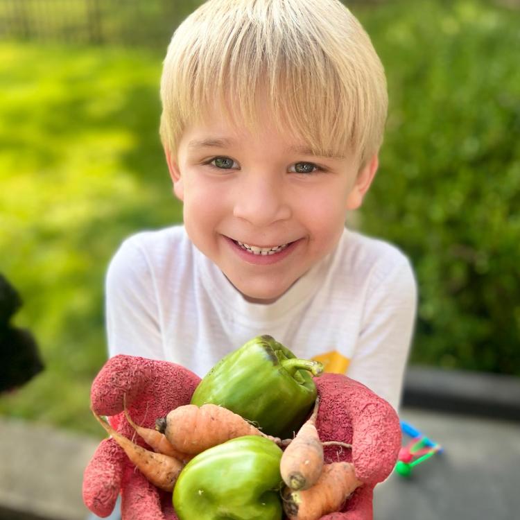 smiling blond boy holds up his hands, full of carrots and peppers