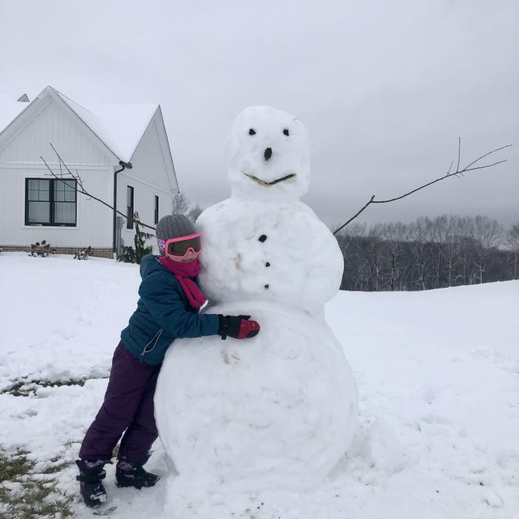 child hugs giant snowman