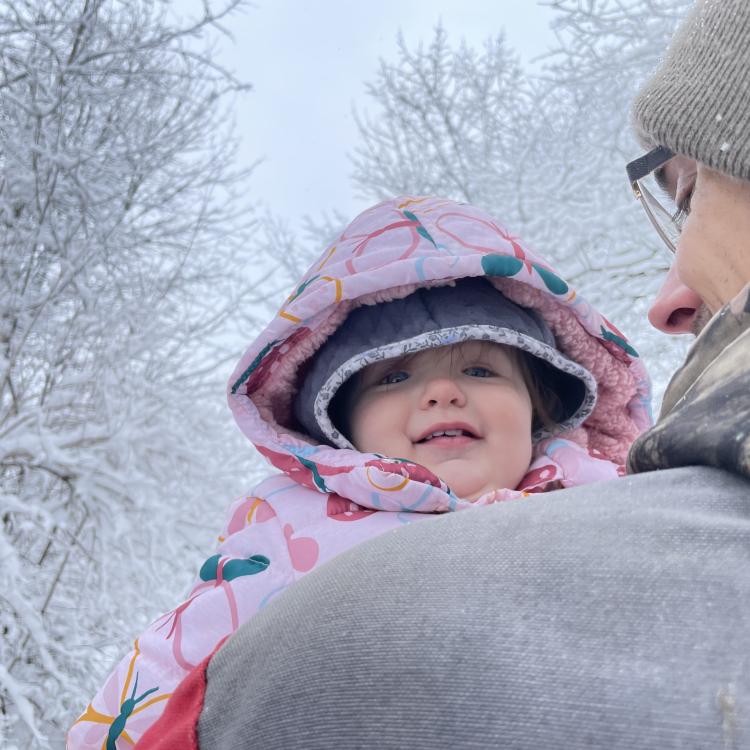 little girl looking over man's shoulder in front of snowy trees