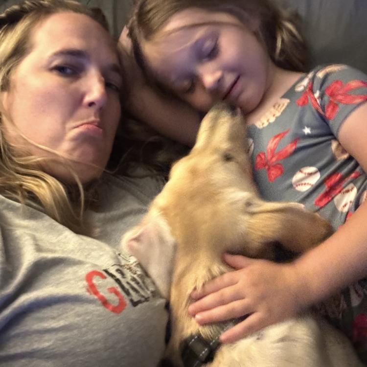 Woman, girl, and dog snuggled on couch