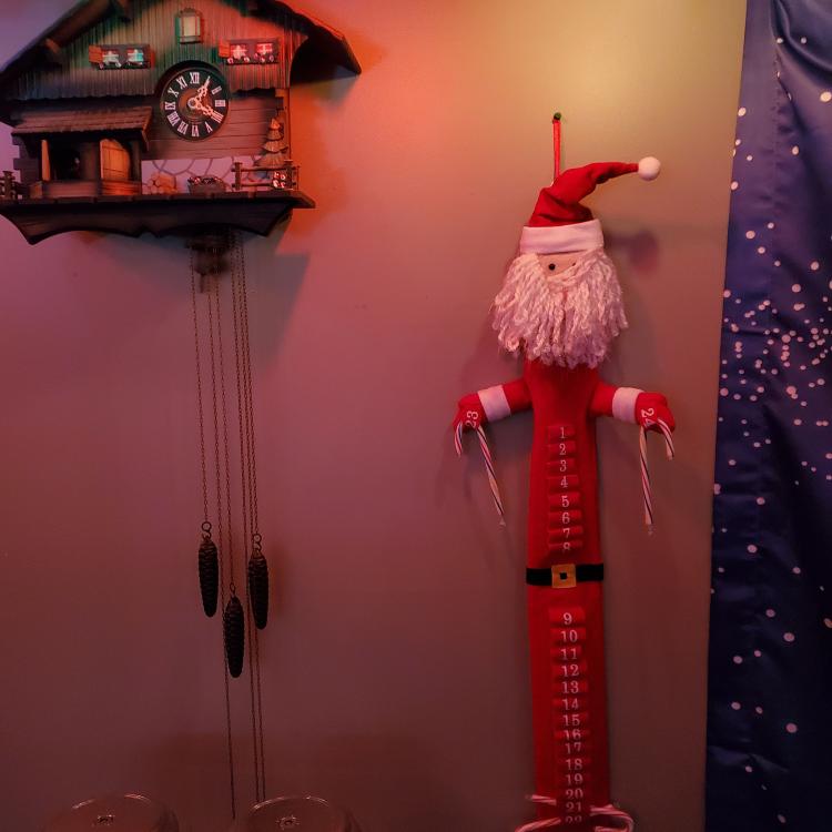 Long fabric Santa Advent Calendar, with two candy canes left at the bottom, hangs on the wall beside cuckoo clock.