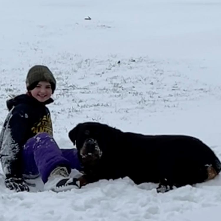 Girl sitting and dog lying in the snow.