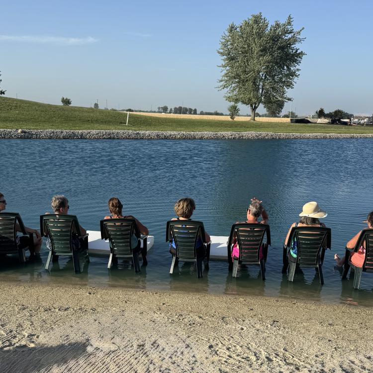 people sitting in chairs in shallow water along lake's edge