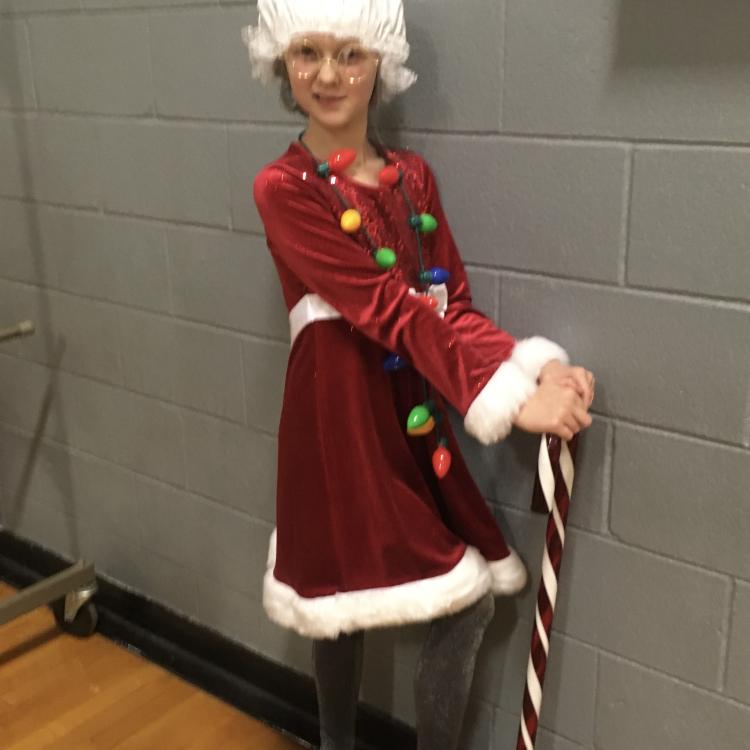 Girl in white-trimmed red dress, wearing Santa hat, leans against cane-sized candy cane