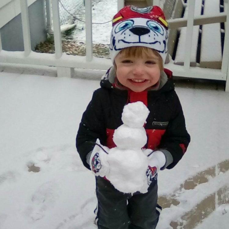 small child on snowy deck holding tiny snowman