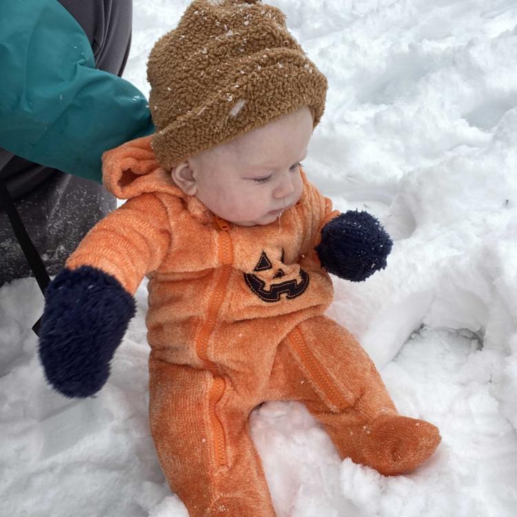 small baby in pumpkin outfit sitting in the snow