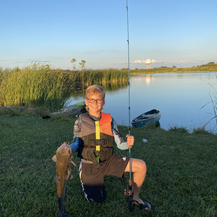 smiling boy kneels while holding fish and pole