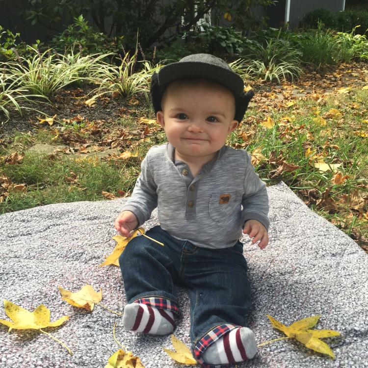 smiling baby sits near fallen leaves