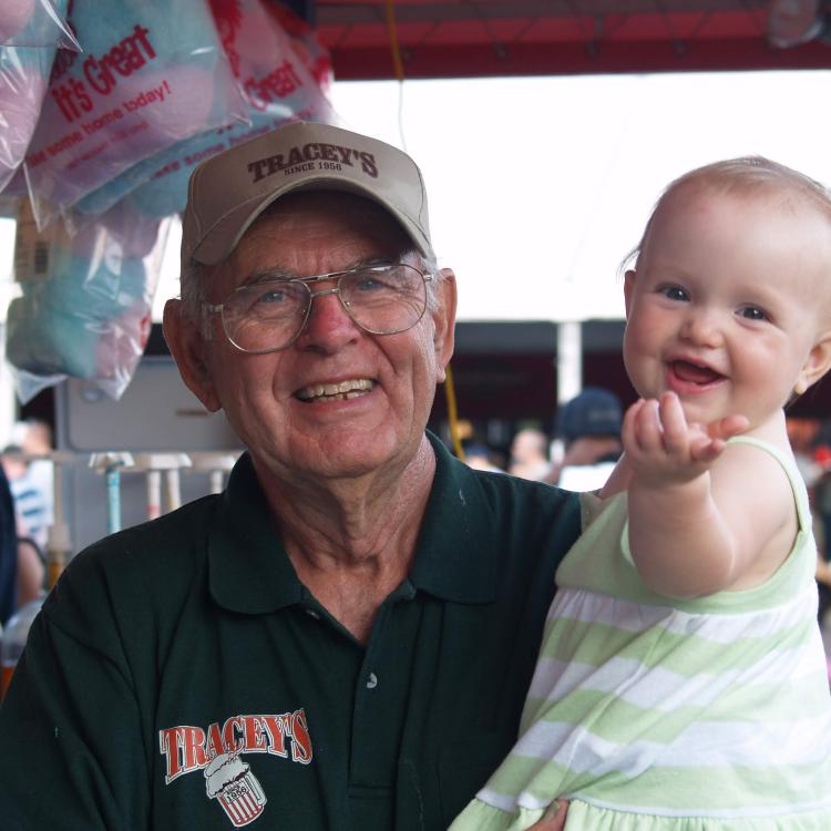 Older man in hat holds smiling baby in front of cotton candy