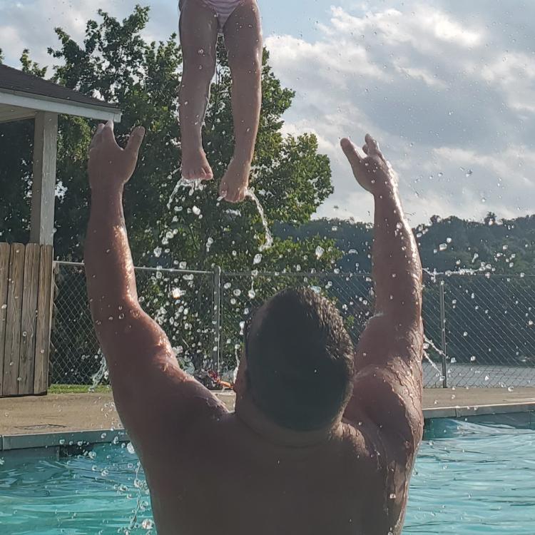 man tosses little girl in air above pool