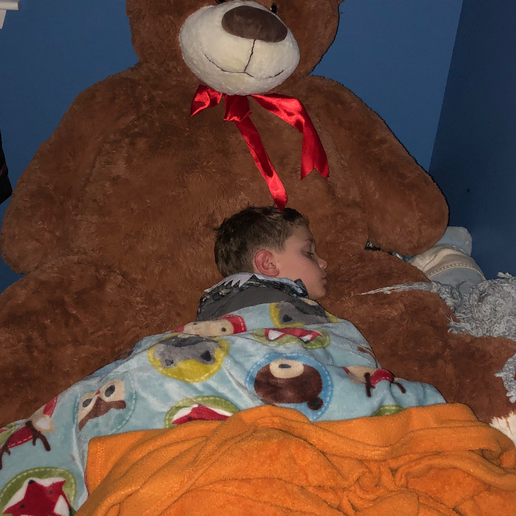 Small boy sleeping against giant teddy bear