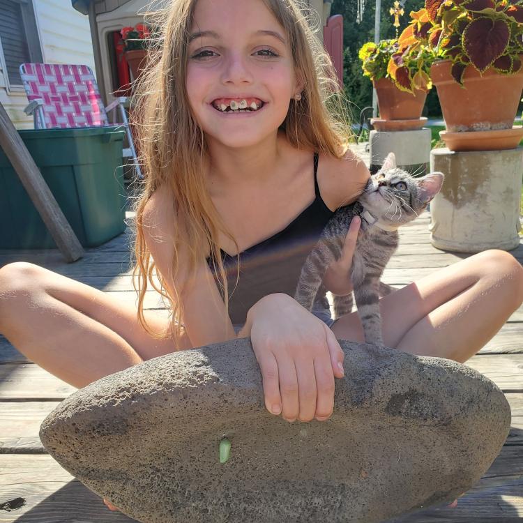 Smiling girl holds cat in one hand and edge of large rock with cocoon on bottom with the other