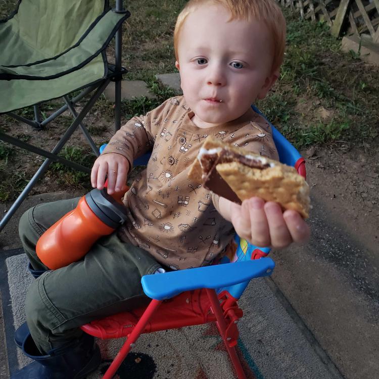 toddler boy on folding chair holds up s'more