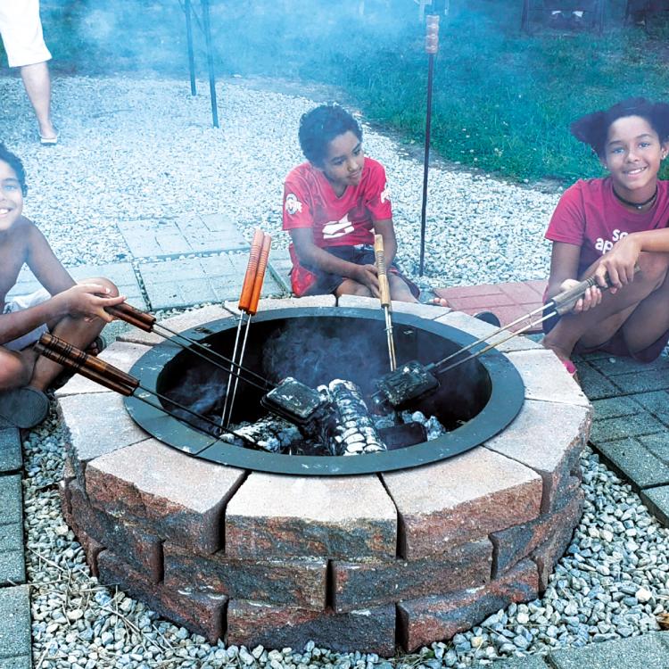 three smiling children roast marshmallows over a campfire