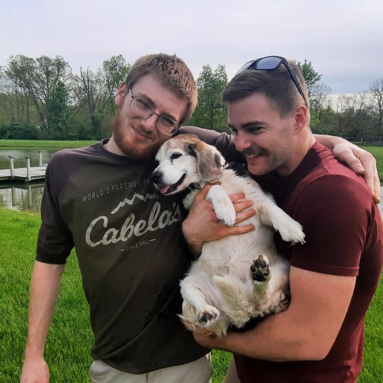 two young men holding a smiley dog