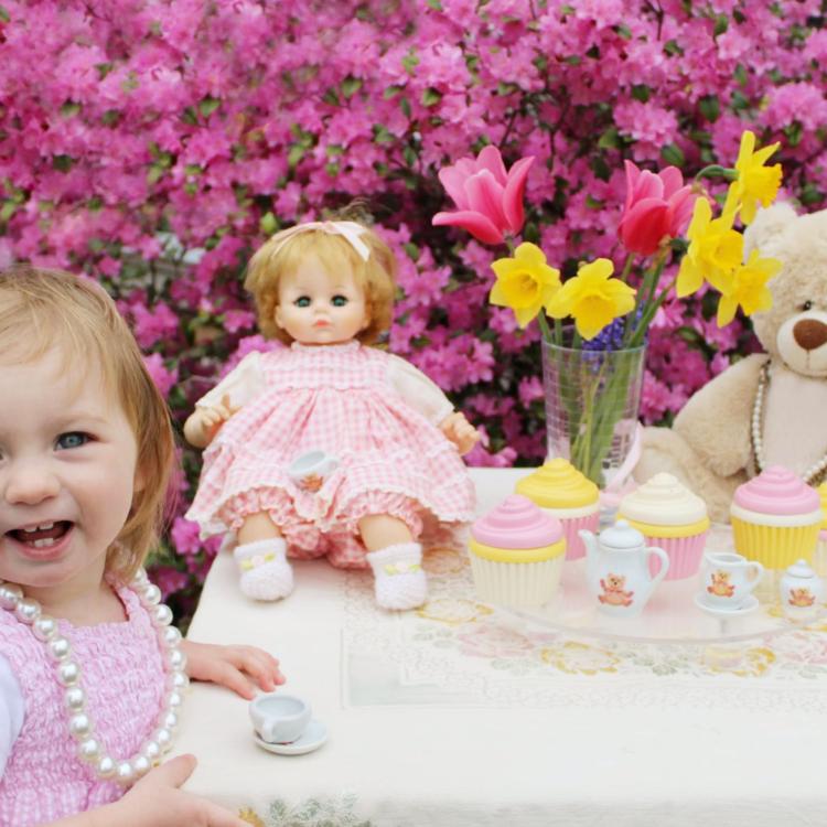 little girl at table with tea set, doll and teddy bear