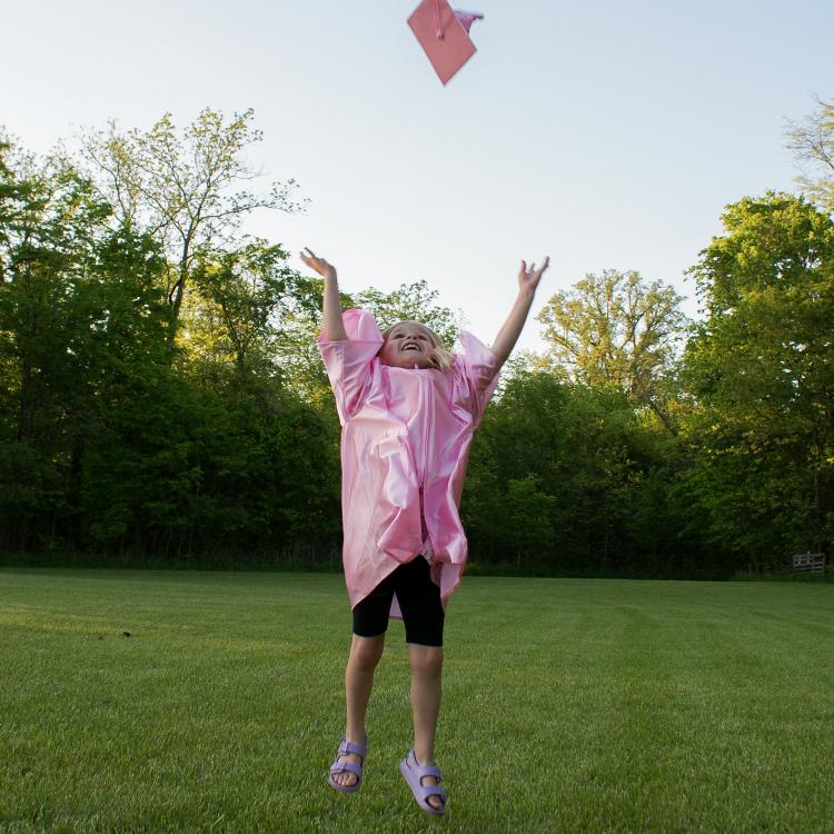 little girl tossing pink graduation cap in the air