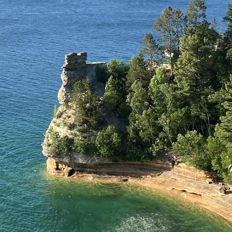 tree-covered rock juts into blue lake waters