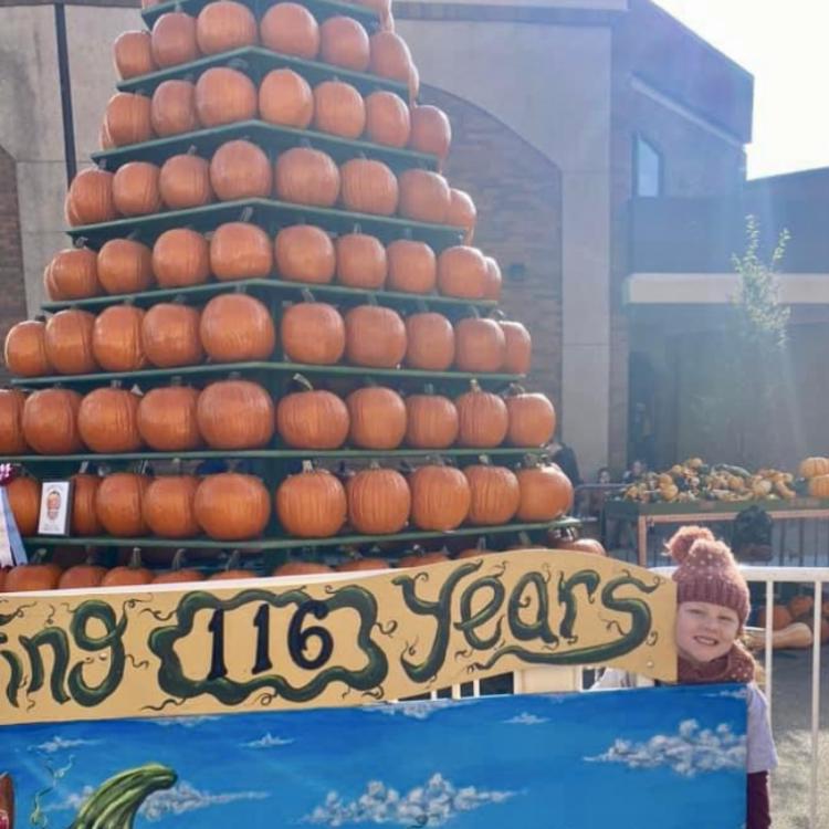 girl peeking around pyramid of pumpkins