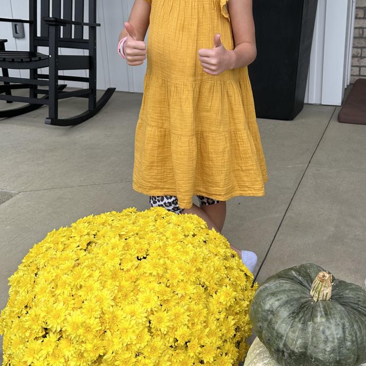 girl in dress behind yellow mum and pumpkin stack