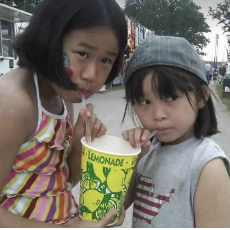 Two girls sip through straws from large cup of lemonade