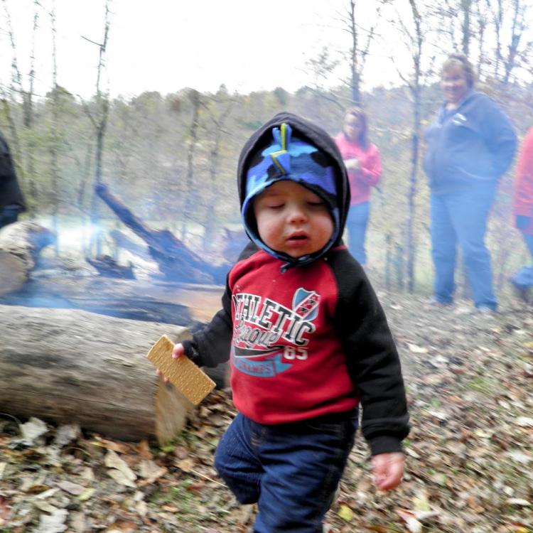 little boy holding graham cracker with campfire in background