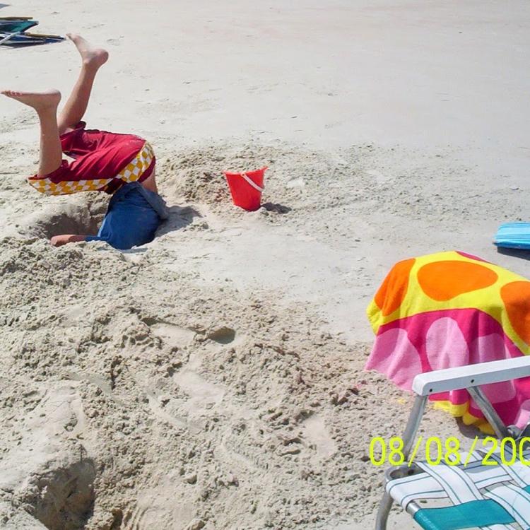 boy's legs stick out from hole in sand