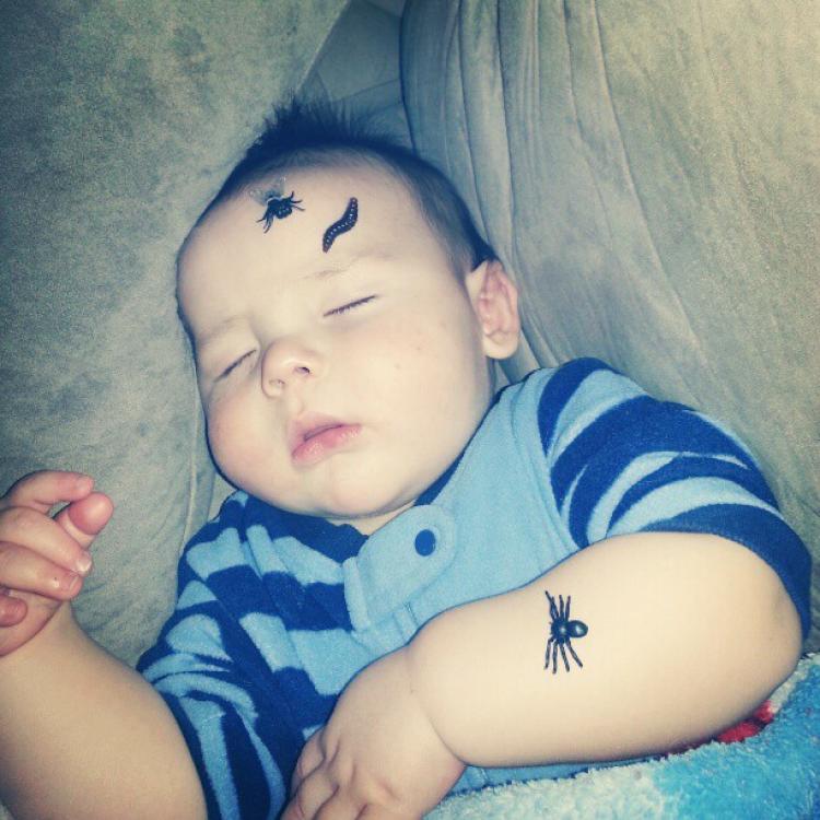 baby sleeping with black spider stickers on his arm and forehead