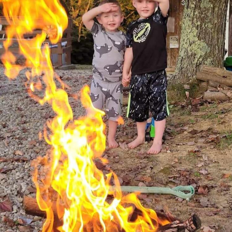 two boys stand behind blazing campfire