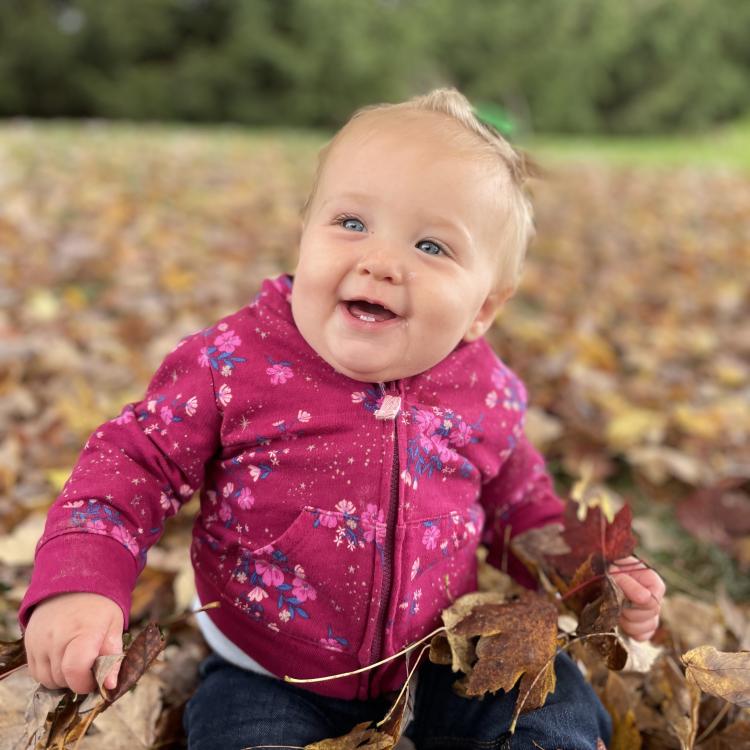 baby in pink jacket sits in leaves