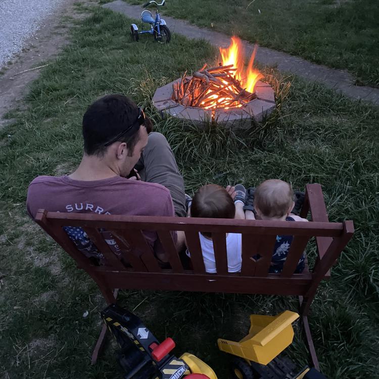 man with two small children on bench by campfire