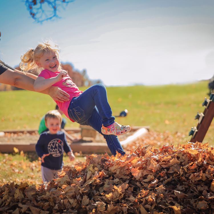 woman tossing little girl into leaf pile