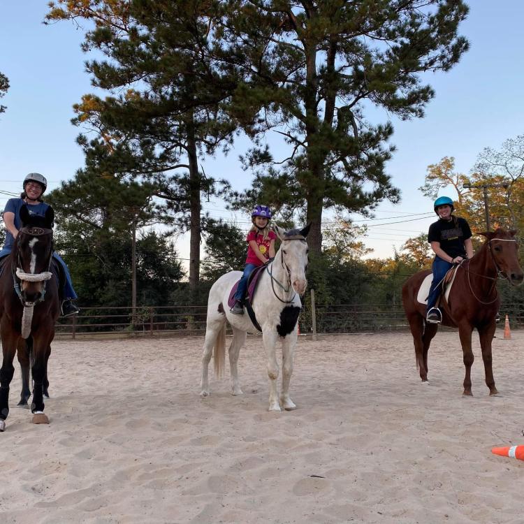 three people on horseback in riding arena