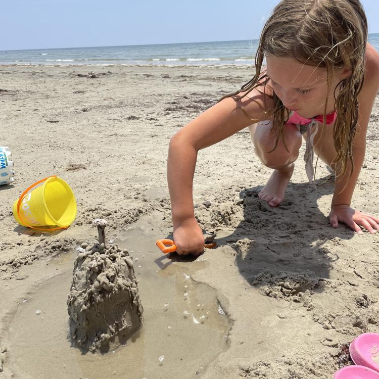 girl next to sandcastle with moat