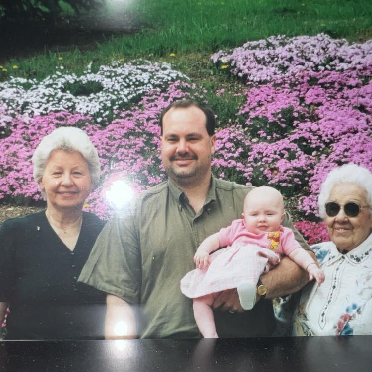 three adults and a baby in front of flower beds