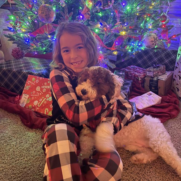 girl hugging dog in front of Christmas tree