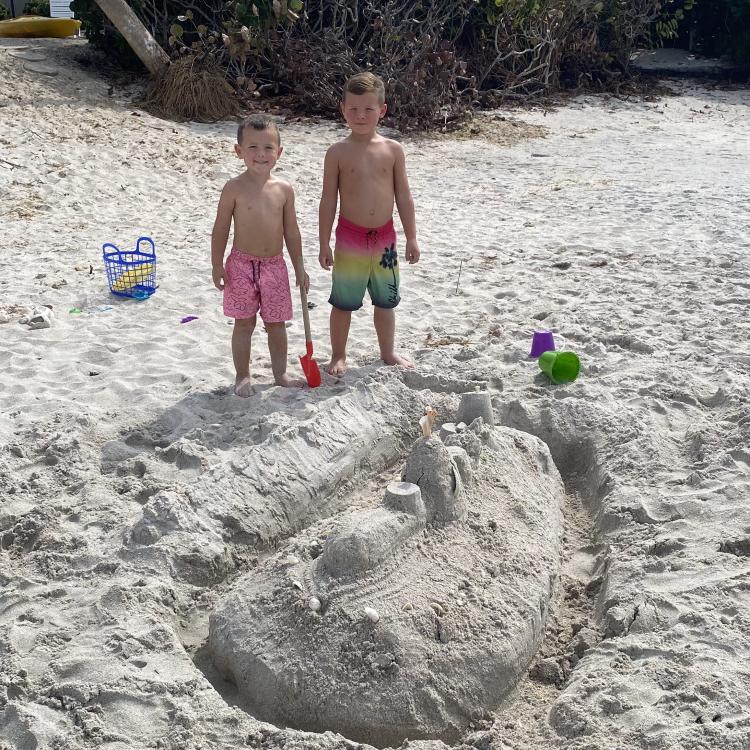 two boys standing behind sandcastle