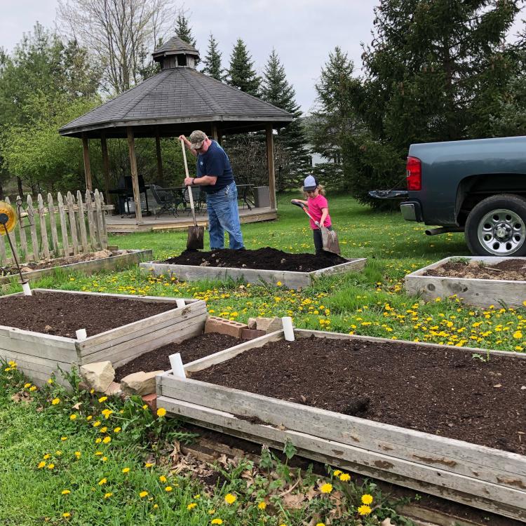 A man and small girl, both wearing hats, shovel soil in wood-framed area