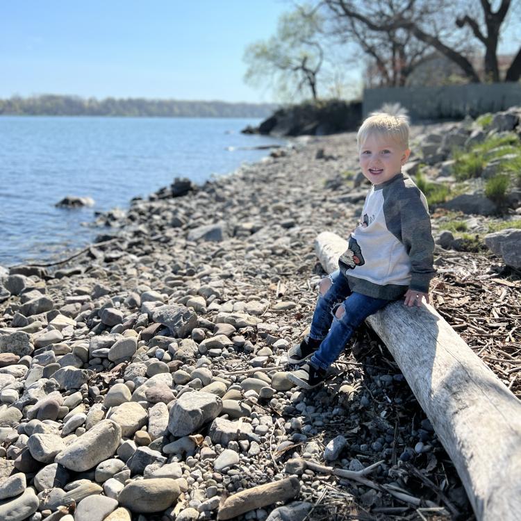 little boy sitting on log by lake