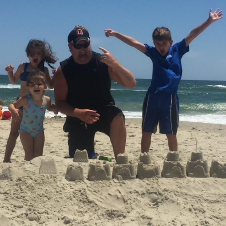 man and three children behind sandcastle
