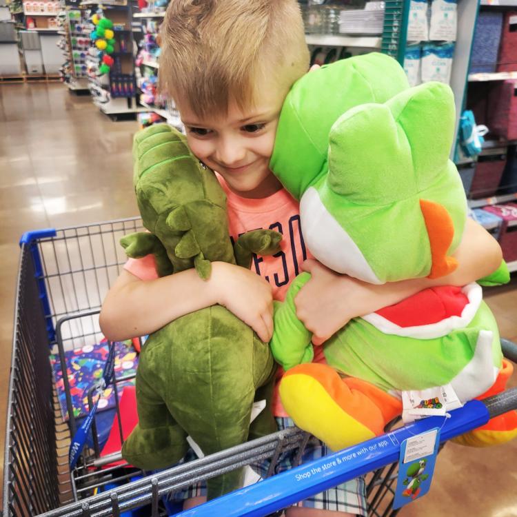 young boy in shopping cart hugging two stuffed animals