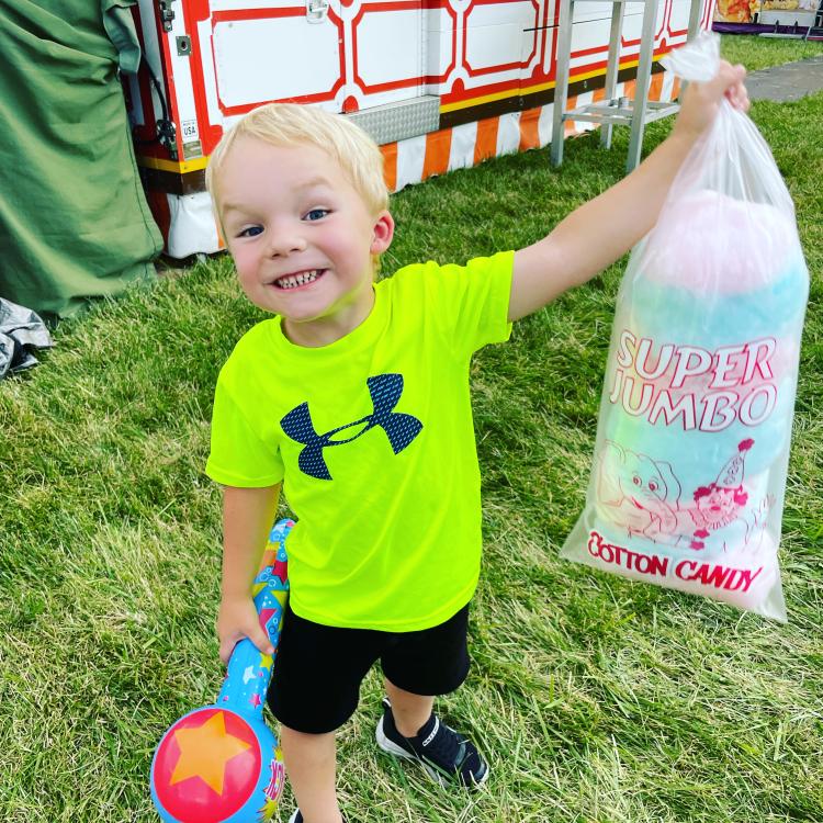 Small boy smiles while holding up a bag of cotton candy