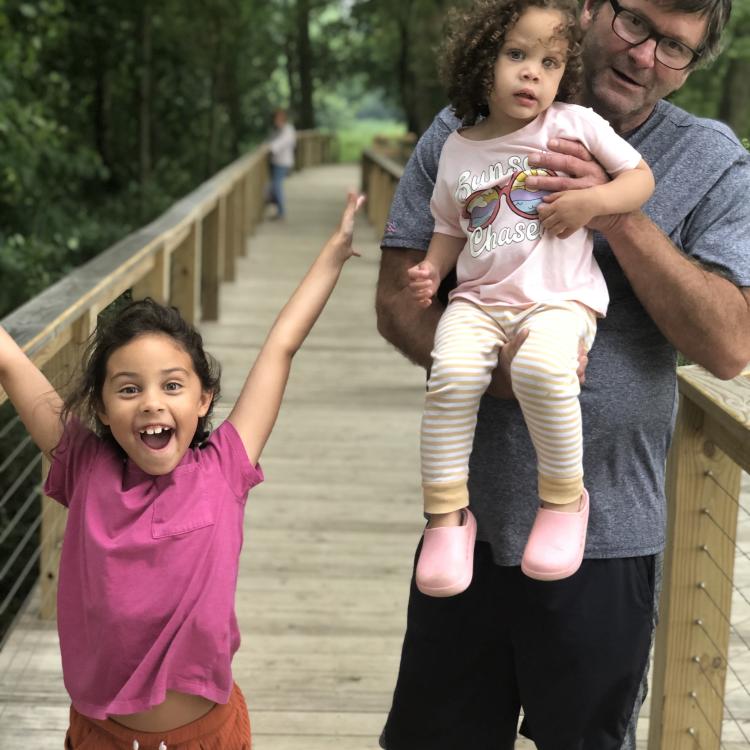 man and two girls on wooden bridge with woods in the background